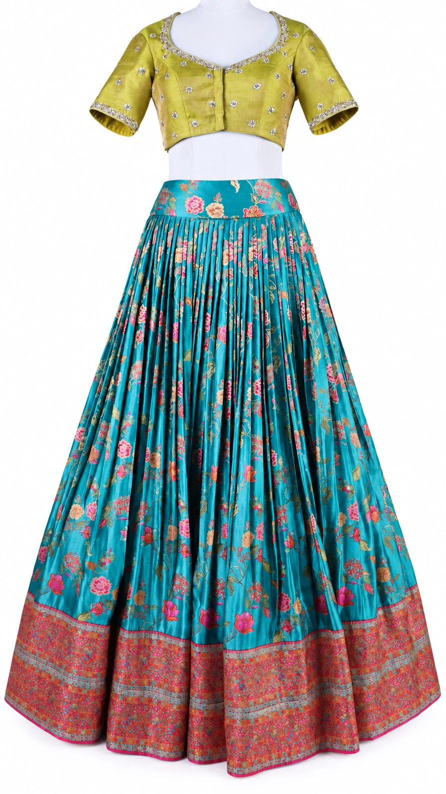 Turquoise florals, fresh green and bright pink bring a vivid contrast to this three-piece lehenga set by Vinisha Rao Designer Studio. The gathered Gaji silk lehenga features multicoloured floral motifs and a broad pink patterned border. The green raw silk blouse has a front button fastening, elbow-length sleeves and metallic floral embroidery around the neckline and cuffs. An open back with tassel ties completes the blouse, while the pink chiffon dupatta adds a soft layer with an embellished scalloped borde